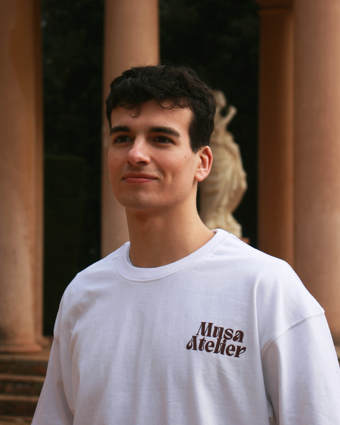 Person wearing a white t-shirt with text on the back, standing in a minimalistic room.